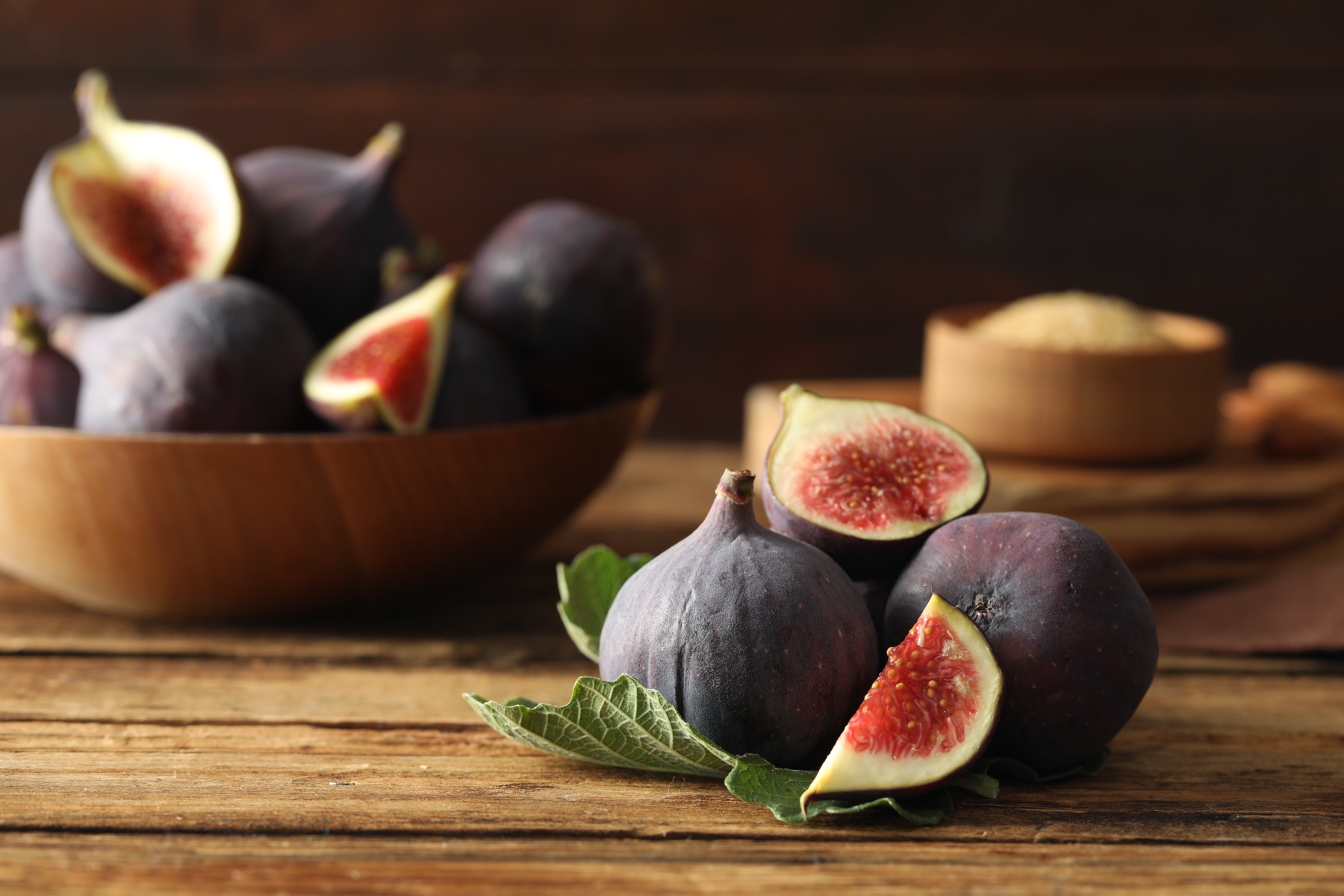 Fresh purple figs, whole and halved, beside a green fig leaf